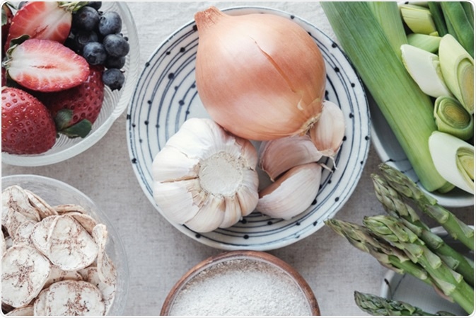 Variety of prebiotic foods, raw green banana, asparagus, onions, garlic, leeks, berries and green beans. Image Credit: SewCream / Shutterstock