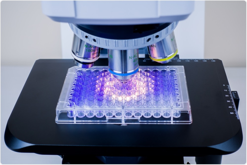 Microscope shining fluorescent light on 96-well plate containing cells