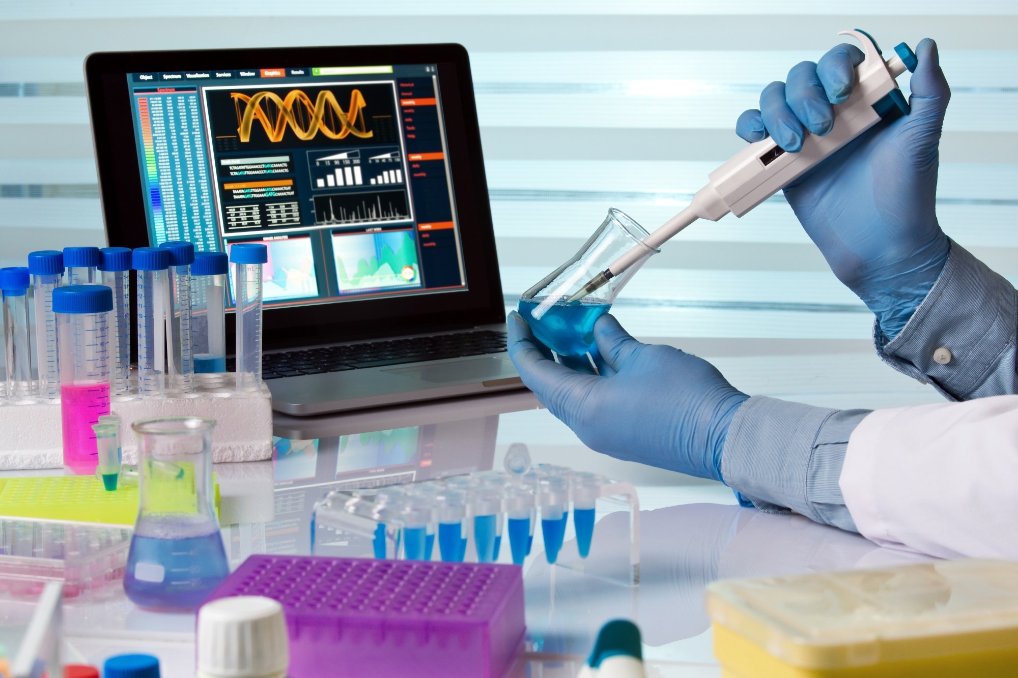 Scientist holding flask and working with laptop in lab