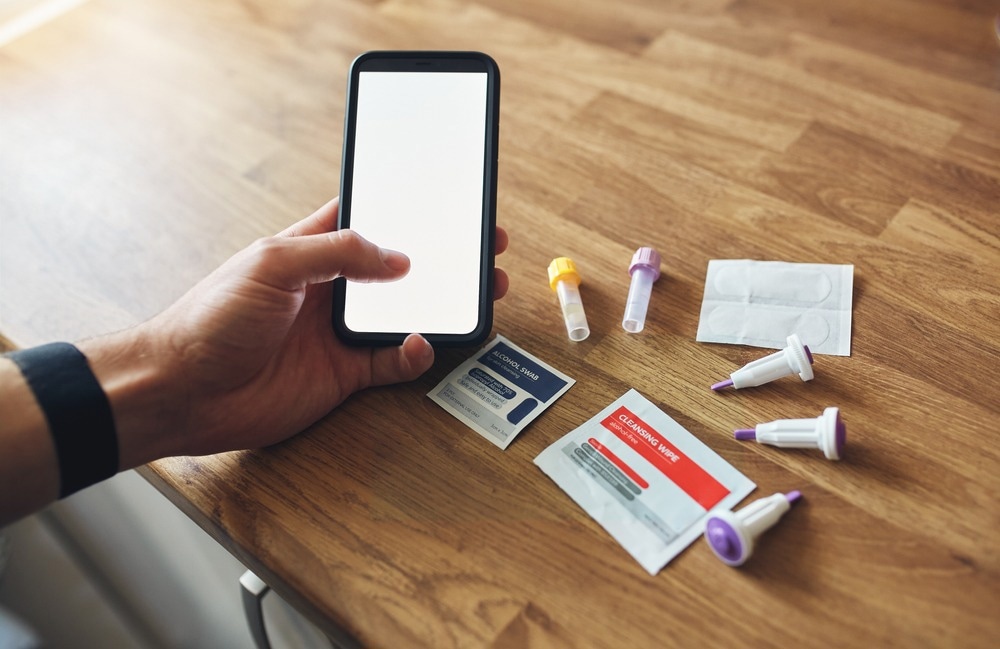 Home blood test kit with blank phone screen on wooden table in mans hands.