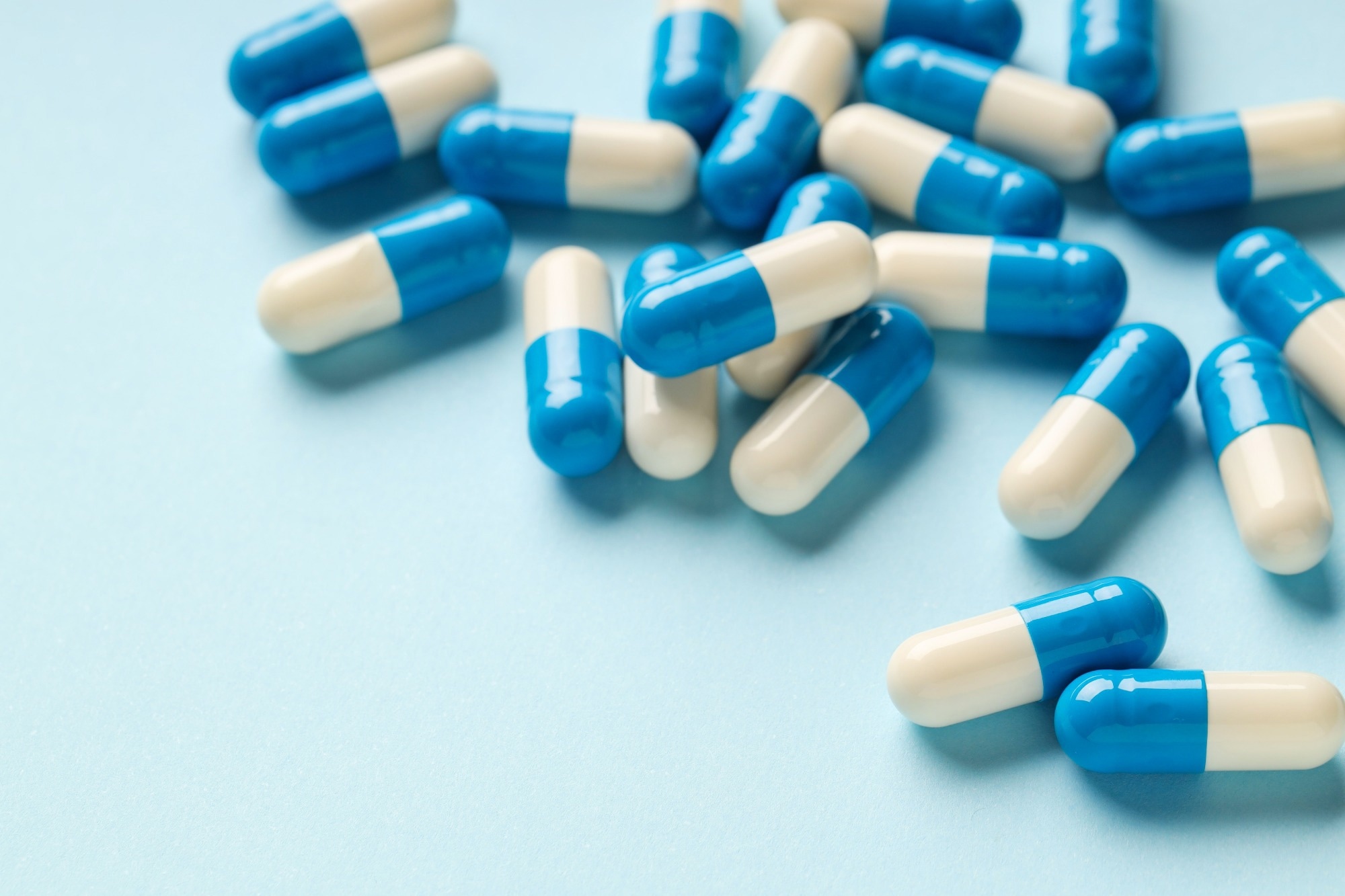 Many antibiotic pills on light blue background, closeup.