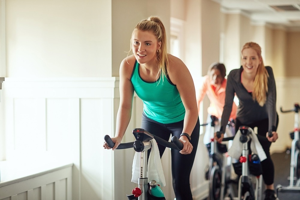 Female person, riding and stationary machine for workout challenge, aerobic instructor and equipment