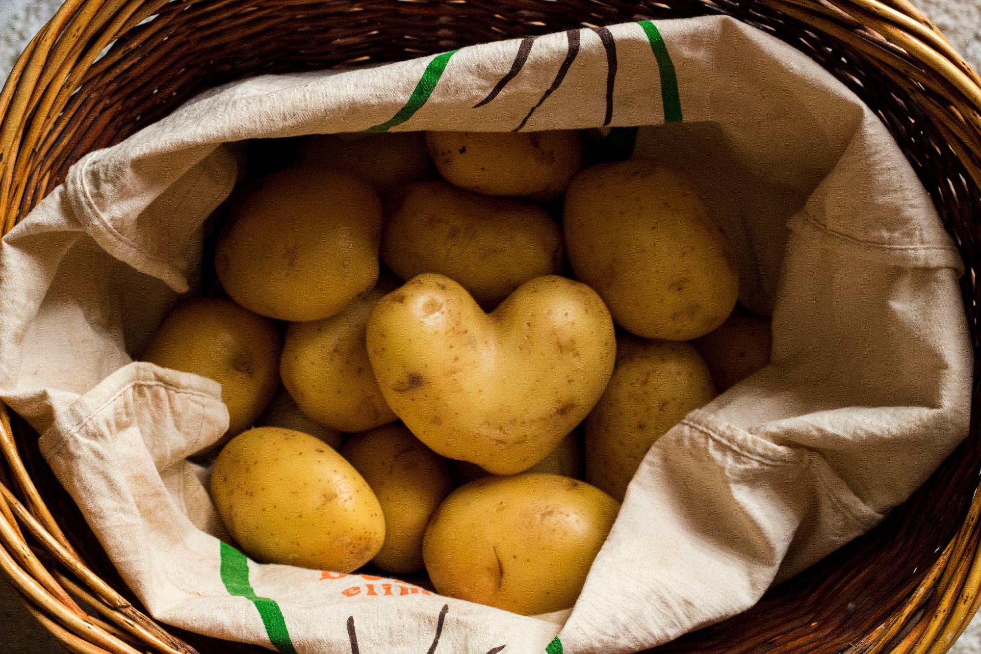 Heart shaped potato in a basket that full of potatoes.