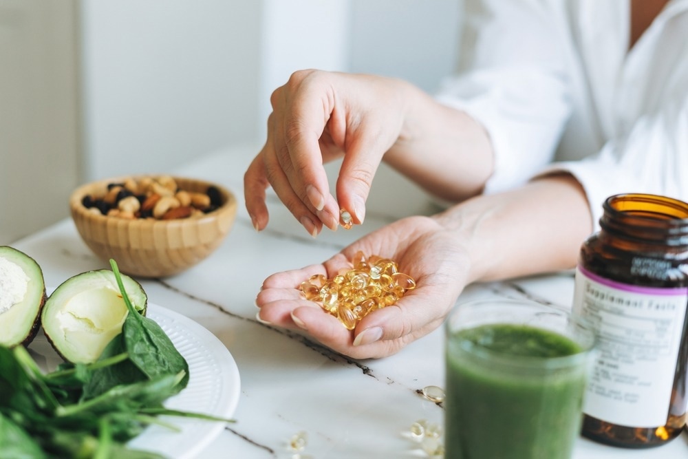Woman doctor nutritionist hands in white shirt with omega 3, vitamin D capsules with green vegan food.