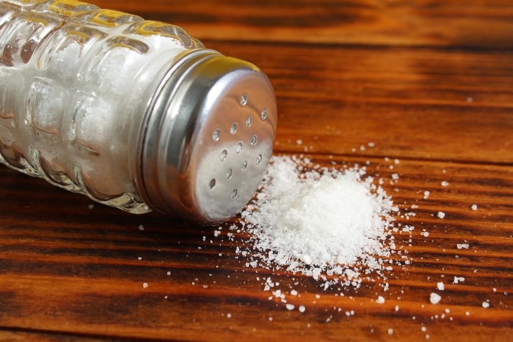 On a wooden table lies a glass salt shaker with overturned salt.