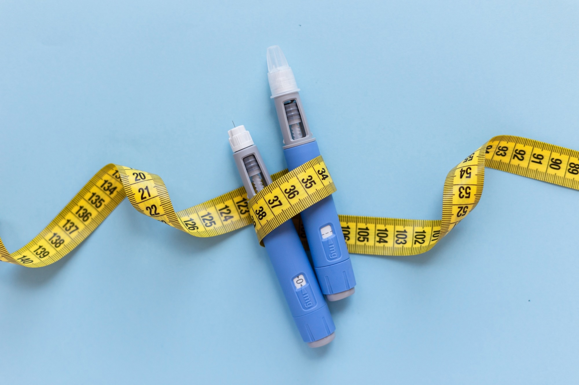 Two injectors dosing pens for subcutaneous injection of antidiabetic medication or anti-obesity medication hovering over a blue background.
