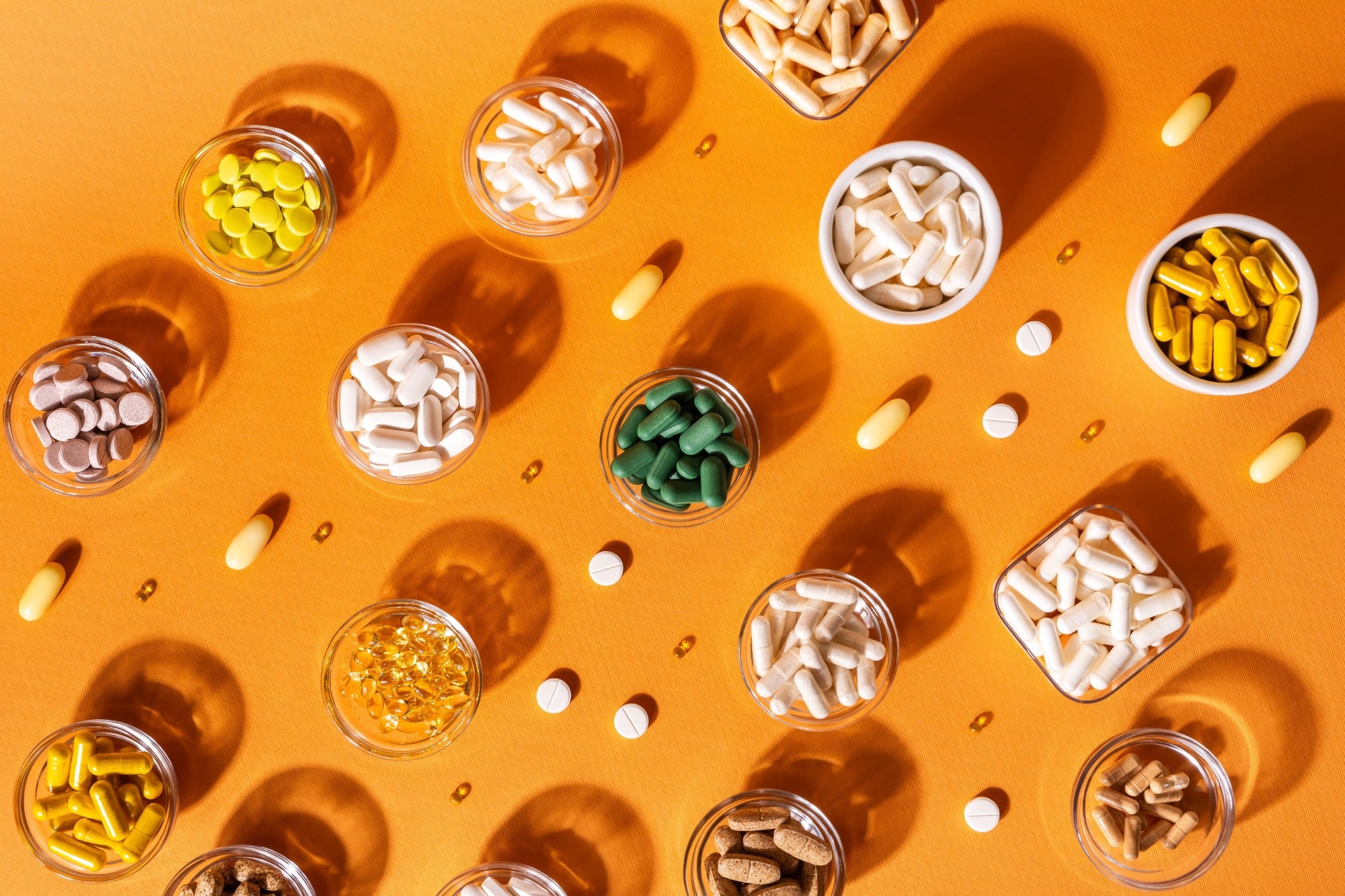 Organic dietary supplements, many capsules of vitamins and minerals in small bowls from above on an orange background.