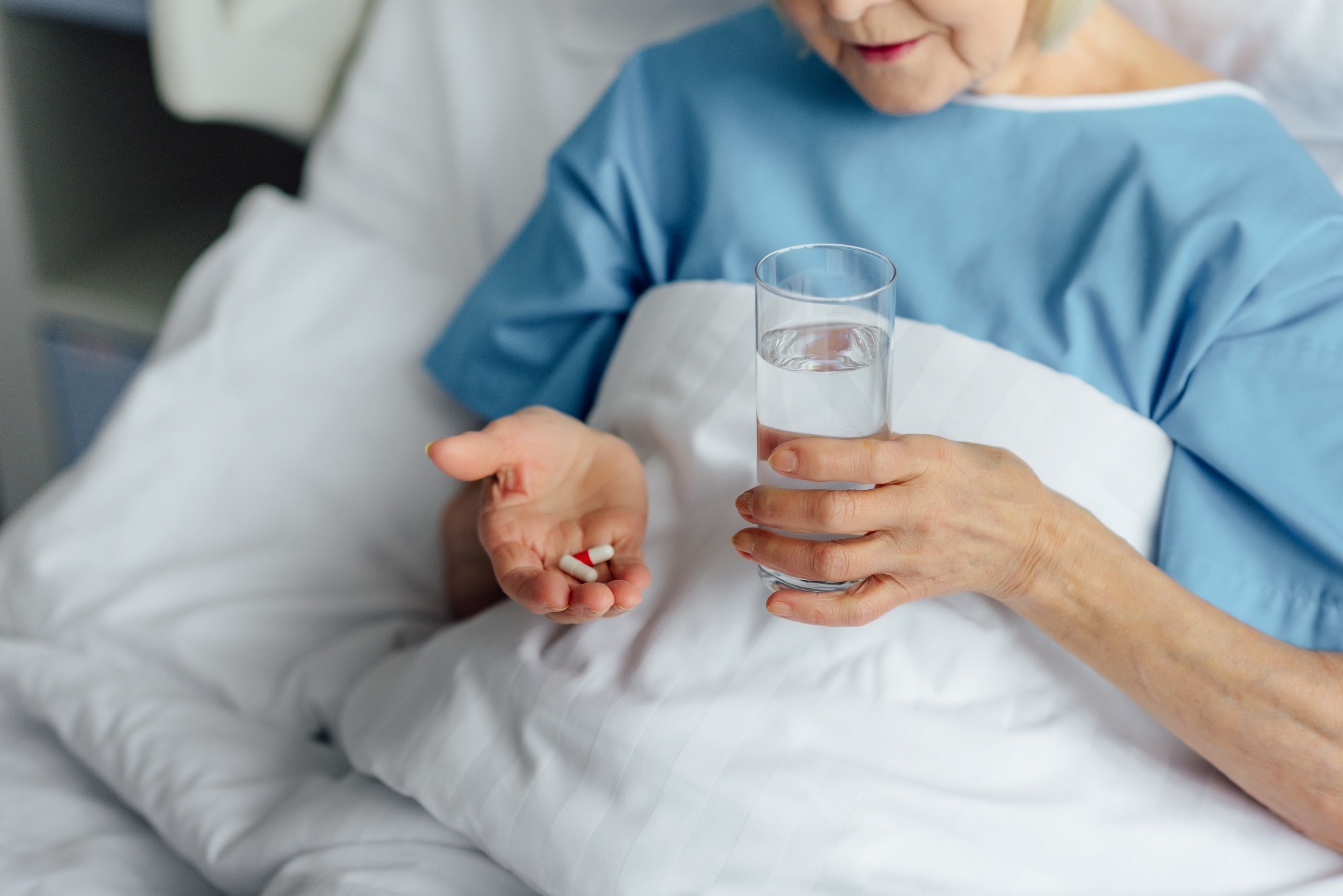 woman lying in bed and holding pills with glass of water in hospital