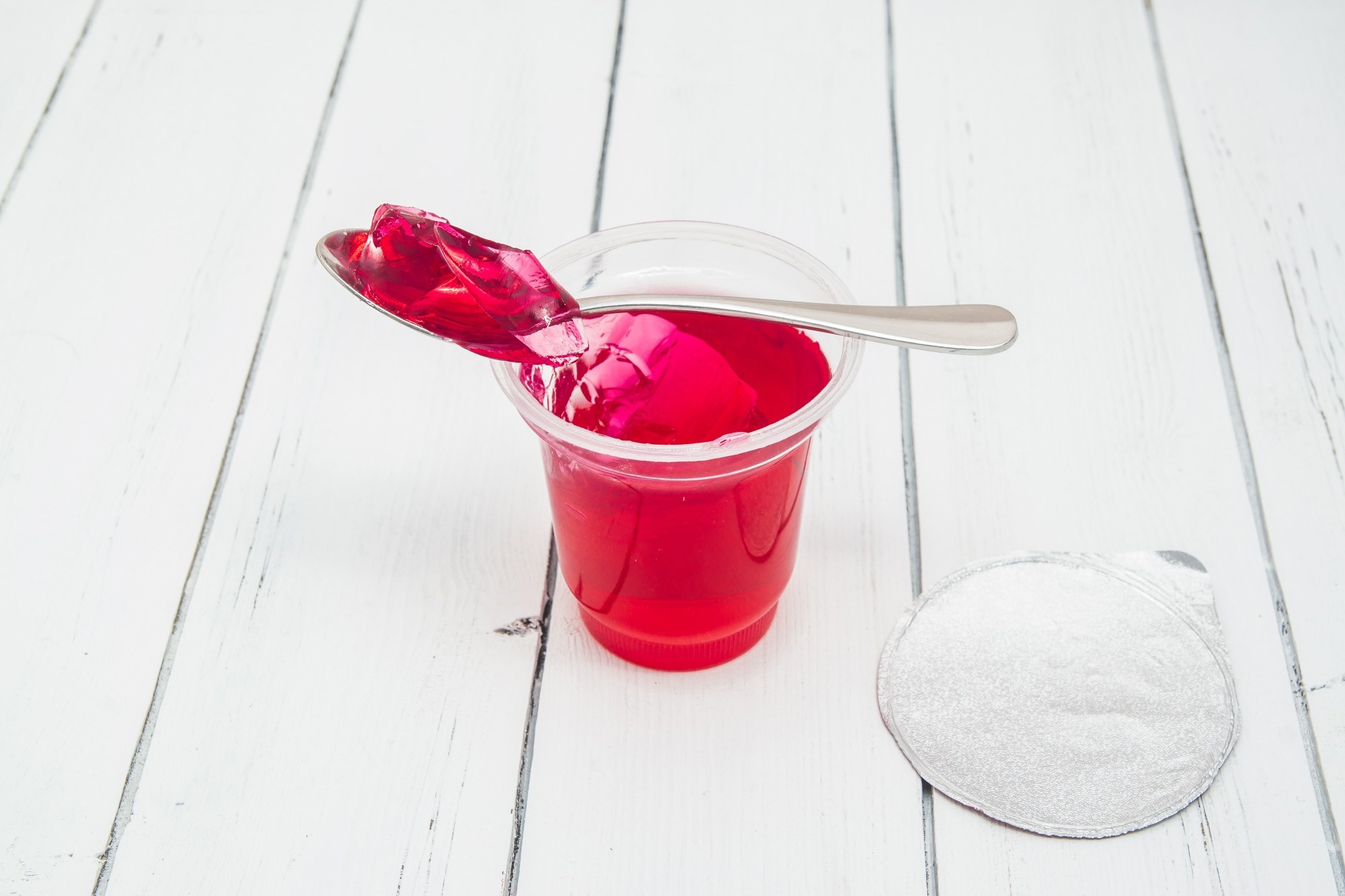 Plastic container for dairy foods with red clear jelly pudding with foil lid and spoon