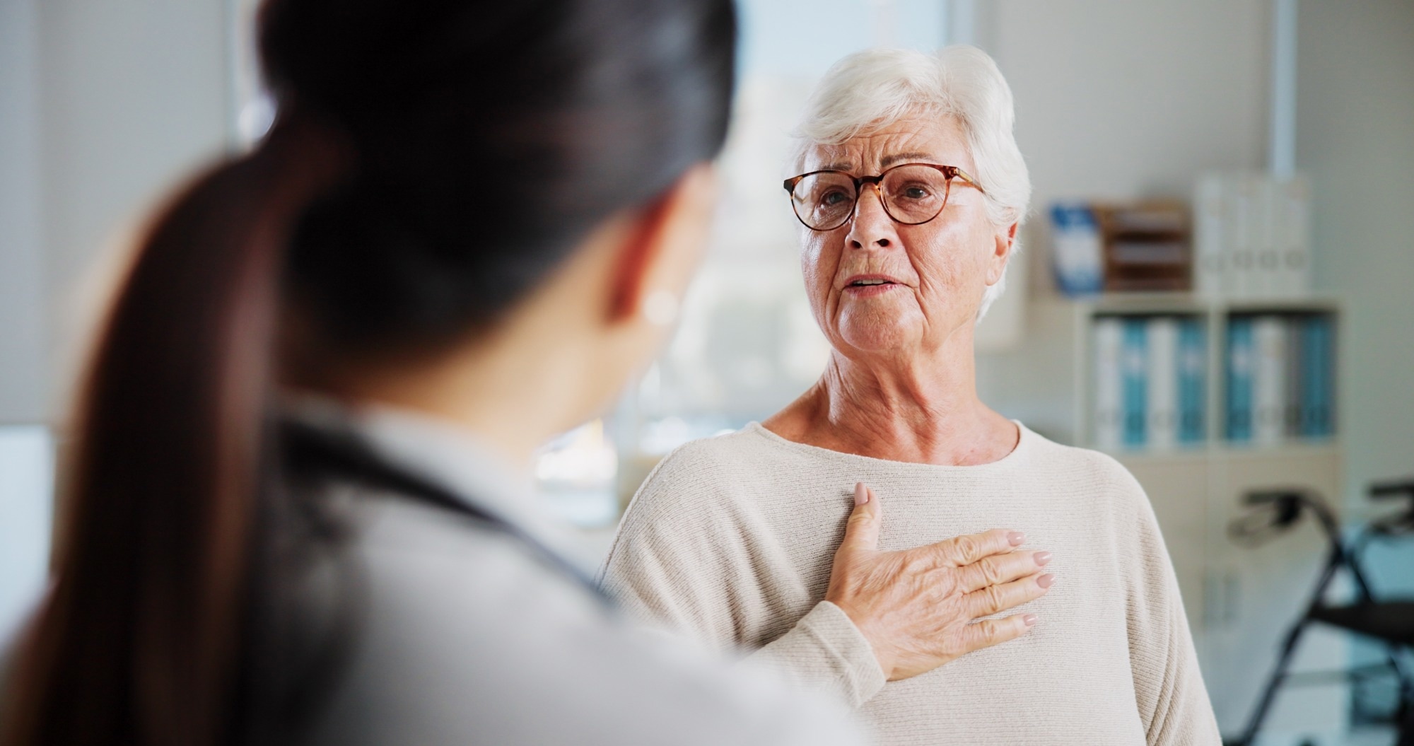 Elderly lady holding chest in pain whilst talking to a healthcare worker