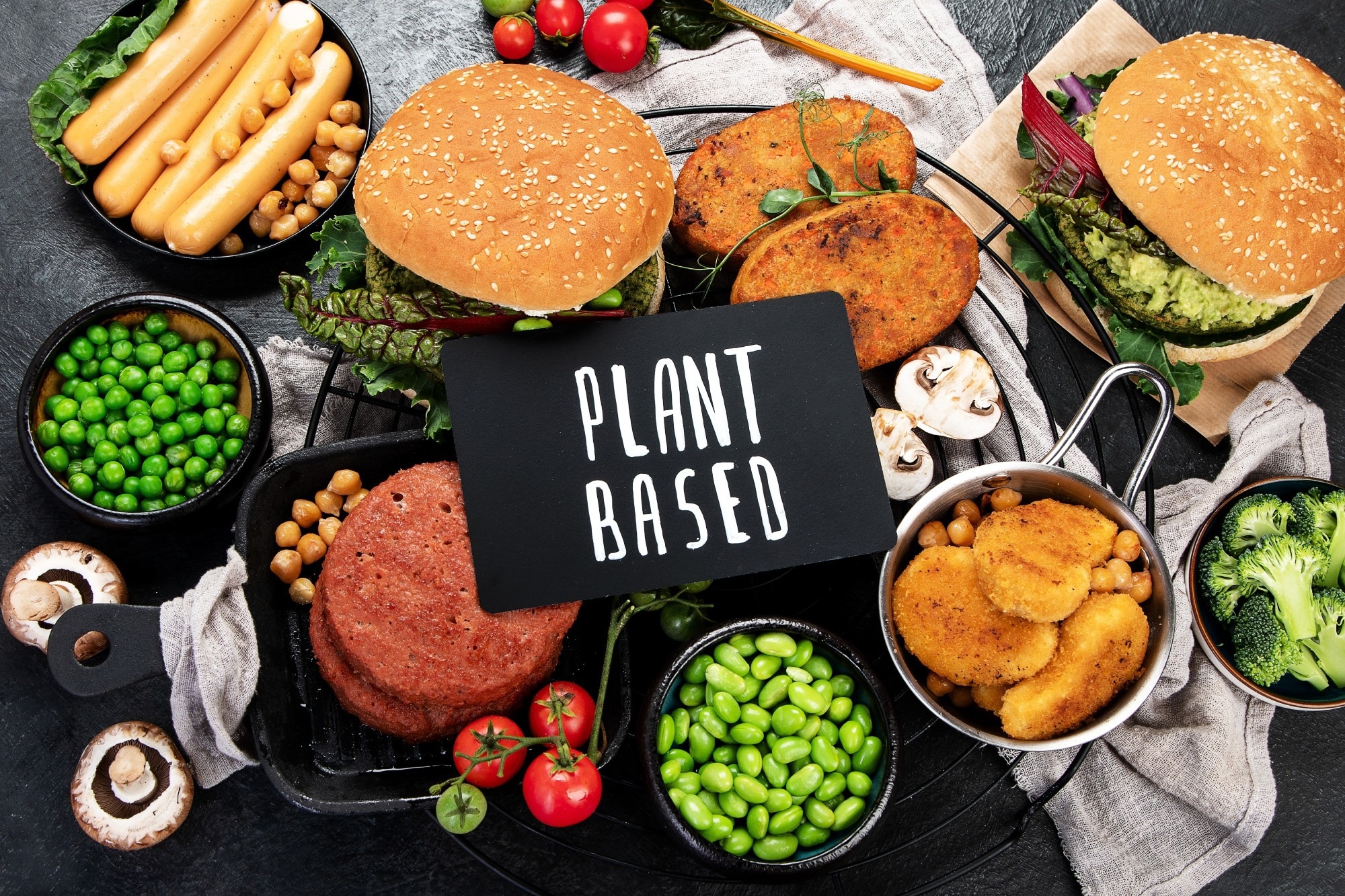 Plant-based food concept-vegan burgers, sausages, vegetarian nuggets, fresh vegetables and sauces on a dark background. top view