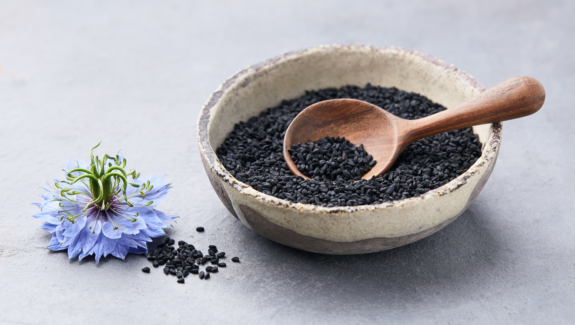 Black cumin seeds with nigella sativa flower on grey background